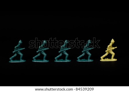 A line of toy soldiers stood against a black background. They are marching in line with a soldier from the opposition leading them. Conceptual Image with a nice strong contrast.