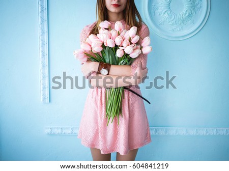 Beautiful young woman in pink dress with spring pink flowers on the blue background in the morning.