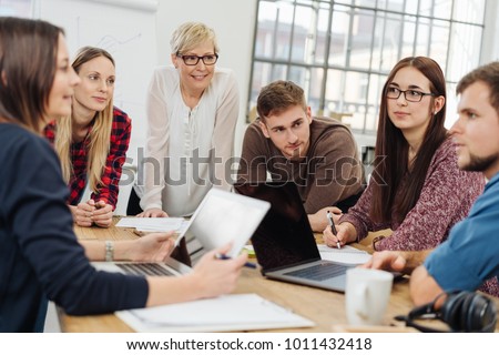 Group of diverse young adults in a meeting with a manageress or university tutor sitting grouped around a table in a bright spacious office