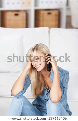 Smiling woman sitting on the floor and calling on her mobile phone