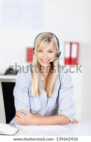 Young blonde call center agent sitting against the blurred background