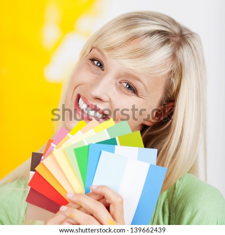 Gorgeous blonde woman holding up a selection of beautiful new paint colours on swatches when renovating and decorating her house
