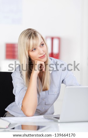 Attractive young blond woman sitting at her laptop staring off into space contemplating her business strategy