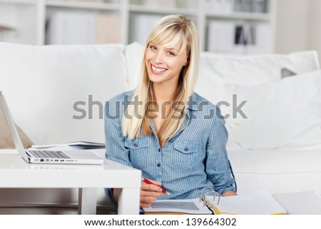 Portrait of a young woman browsing the Internet on her laptop and writing on the folder while sitting on the floor at home indoor
