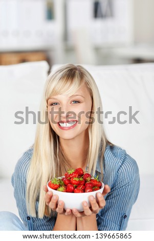 Smiling attractive young blonde woman with a bowl of delicious ripe red strawberries held in her hands