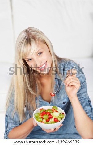 Happy beautiful young woman full of vitality eating a bowl of fresh diced fruit salad for a healthy diet