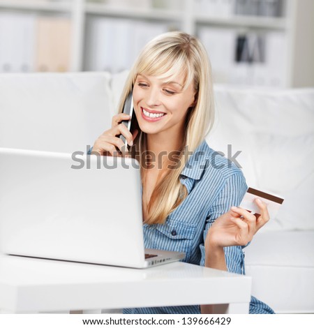 Woman calling and holding a credit card in front of her laptop