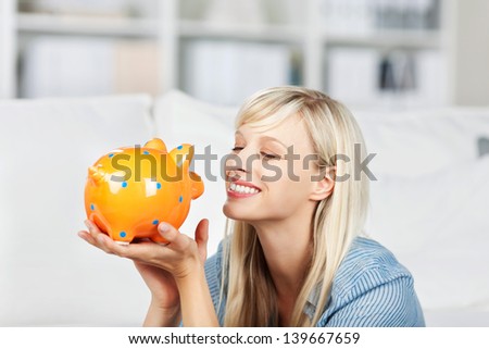 Smiling woman looking at her colourful yellow piggy bank dreaming of what she will do with her savings