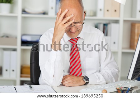 Upset mature businessman with hand on head sitting at office desk