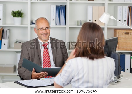 Mature businessman holding CV of female candidate at office desk