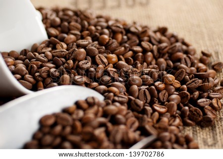 Stainless steel scoop and coffee cup laying in a pile of roasted coffee seed