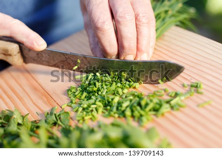 Senior hands cutting fresh chives on the wooden chopping board