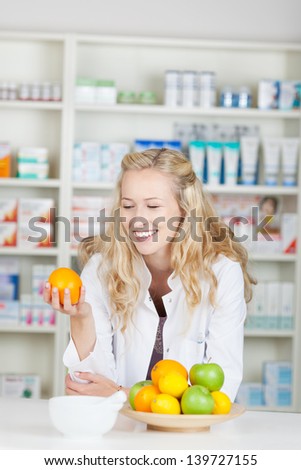 Young female pharmacist holding orange at pharmacy counter