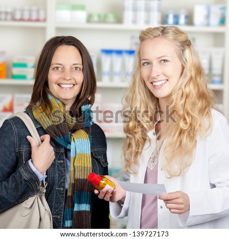 Happy female pharmacist giving medicine bottle to customer in pharmacy