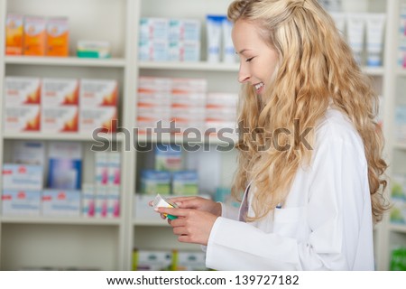Portrait of young female pharmacist with medicine from shelf in pharmacy