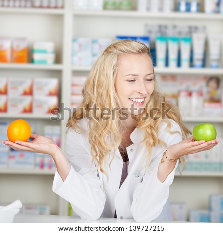 Young female pharmacist comparing apple and orange in pharmacy