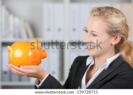 Cute blonde businesswoman holding a piggy bank in her office