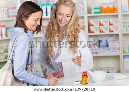 Young pharmacist and female customer reading prescription paper at pharmacy counter