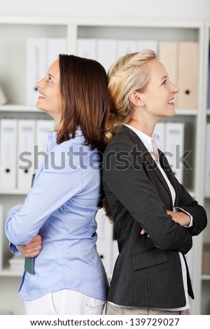 Thoughtful businesswomen with arms crossed standing back to back in office