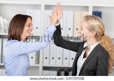 Side view of happy businesswomen fiving high five in office