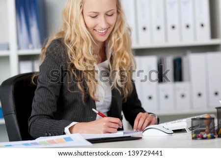 Young businesswoman writing on paper at office desk