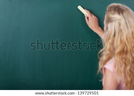 Portrait of happy female teacher writing on chalkboard