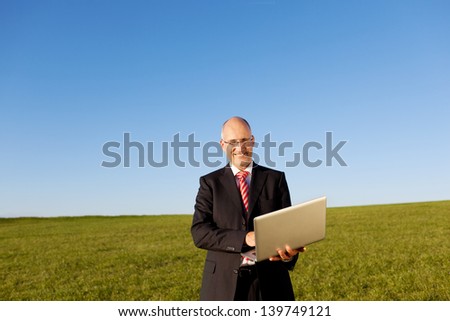 Portrait of mature businessman holding laptop on field against clear sky