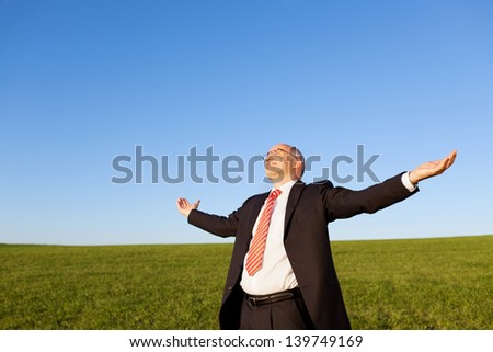 Mature businessman with arms outstretched standing in field against clear sky
