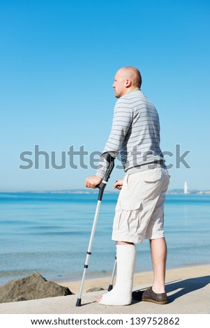 Injured Man with Crutches standing still at sea side