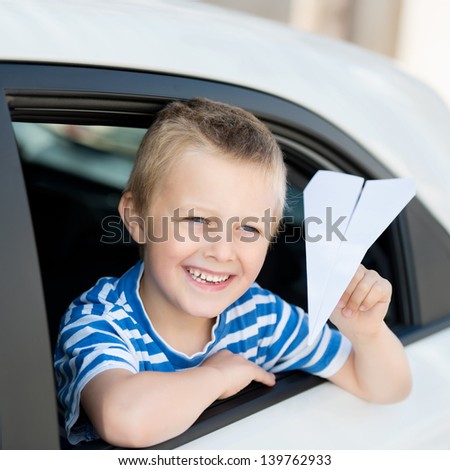 Smiling little boy throwing a paper plane while looking out the car