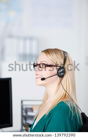 Closeup of young female customer service executive using headset while looking away in office