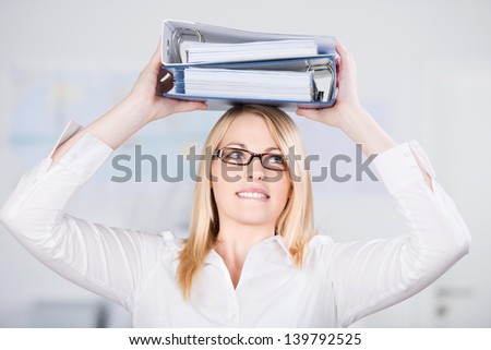 Young blond businesswoman carrying two binders on head in office