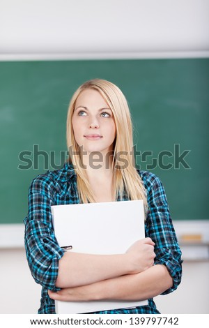 Portrait of female student holding white binder while standing against chalkboard in class