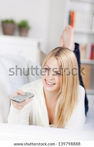 Young woman using remote control while watching TV on sofa at home