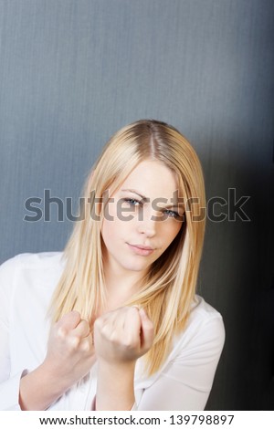 Portrait of an angry young woman with clenched fists isolated over blue background