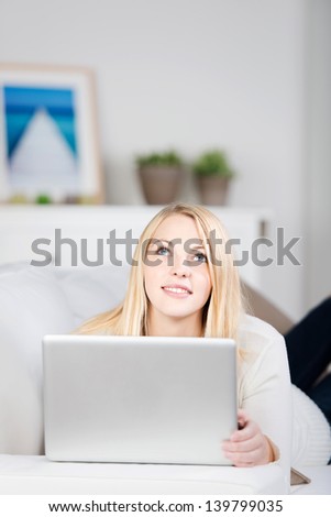 Portrait of young thinking woman with laptop lying on sofa