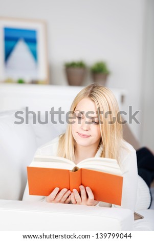 Bright blond woman reading a book on the sofa in the living room