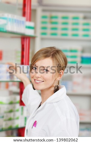 Portrait of young female pharmacist selecting medicine from shelf