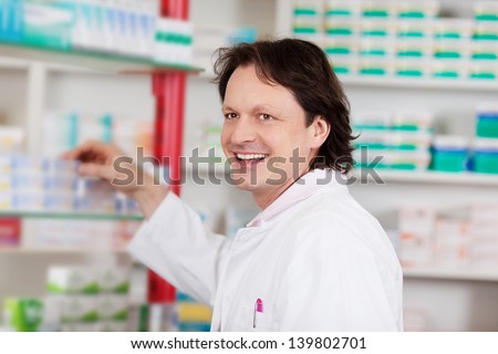 smiling male pharmacist in front of shelf