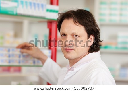 Portrait of mature male pharmacist selecting medicine from shelf