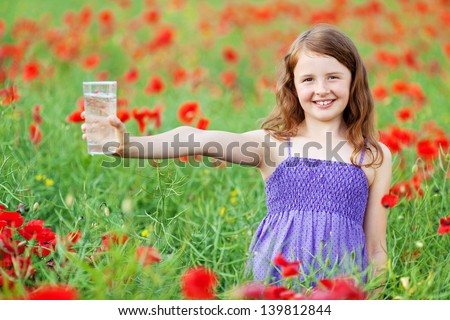 Smiling little child holding a glass of water in flower field