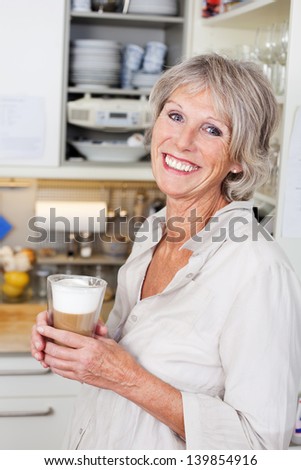 Attracive Modern Elderly Woman Enjoying A Cup Of Cappuccino In Her Kitchen Smiling In Appreciation