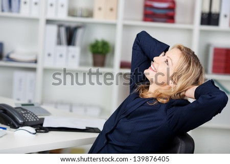 Happy businesswoman relaxing with hands behind head at office desk