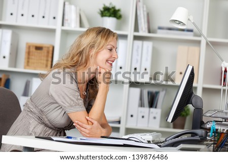 Side view of smiling businesswoman using computer at desk in office