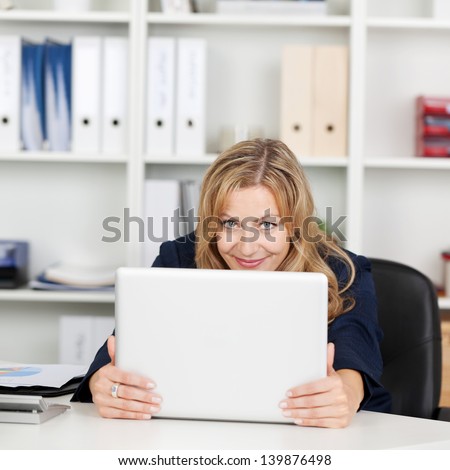 Happy mid adult businesswoman behind laptop at office desk