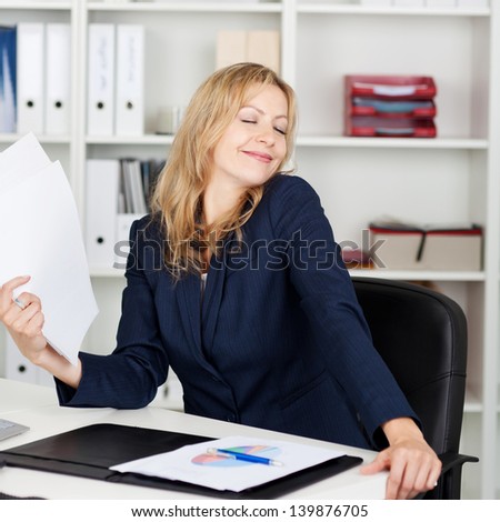 Mid adult businesswoman fanning herself with documents at office desk