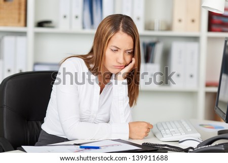 Irritated young businesswoman with head in hands at office desk