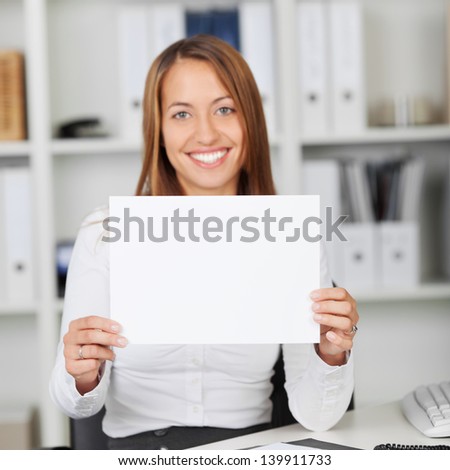 Portrait of happy young woman holding blank paper at office desk