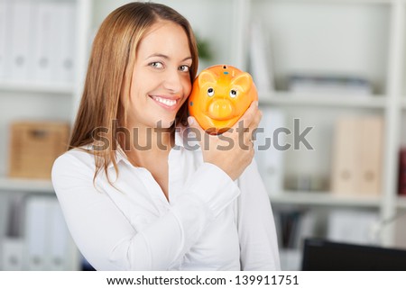 Portrait of happy businesswoman holding piggy bank in office