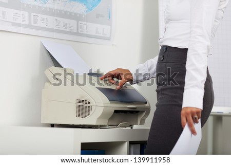 Midsection of businesswoman using copy machine in office